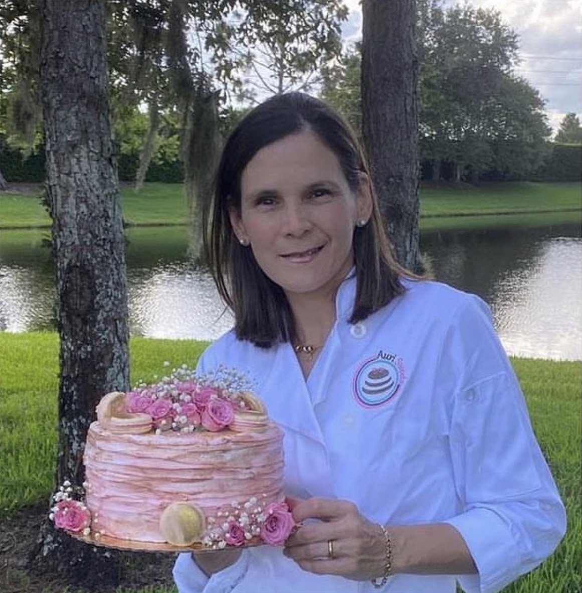 Aura, the baker behind Auri Sweets, holding a pink cake decorated with flowers and macarons