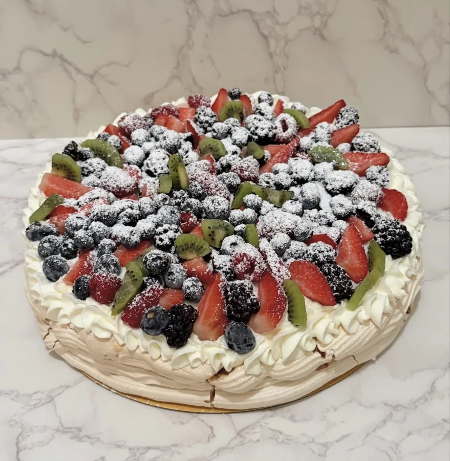 Large pavlova topped with berries, kiwi, and powdered sugar