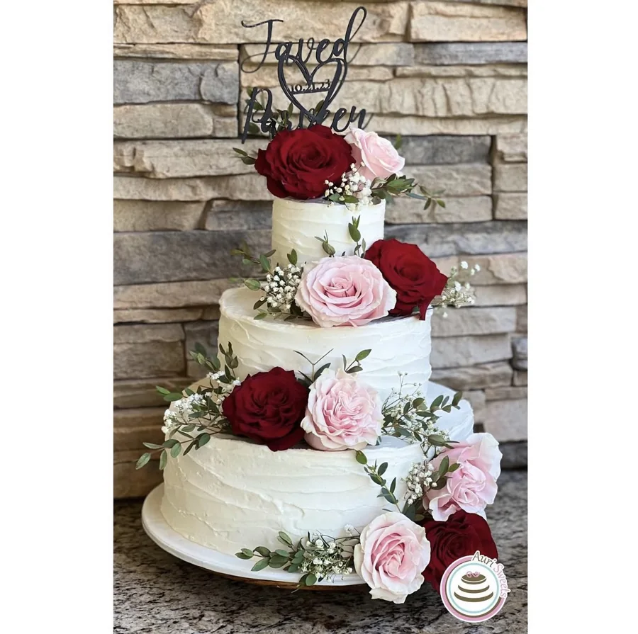 Three-tier white wedding cake decorated with pink and burgundy roses